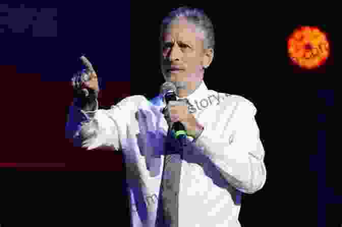 A Photo Of Jon Stewart With A Microphone In His Hand, Standing In Front Of An Audience. Angry Optimist: The Life And Times Of Jon Stewart